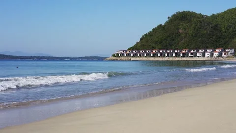 Gentle waves rolling onto a sandy beach with coastal villas and green hills Stock Footage 341947435