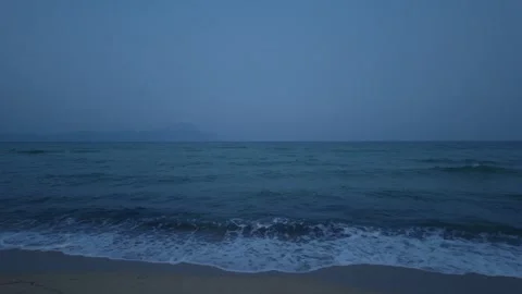 Gentle waves rolling onto a sandy beach at dusk, with the silhouette of Mount Stock Footage 346672522