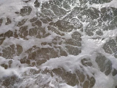 Gentle waves rolling onto sandy beach at sunrise, creating bubbles and a sh.. Stock Photos