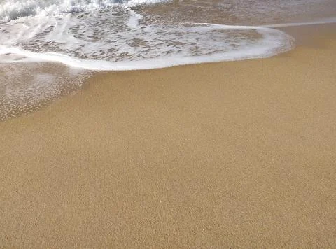 Gentle waves rolling onto sandy beach at sunrise, creating bubbles and a sh.. Stock Photos