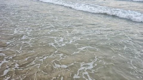 Gentle waves rolling onto a sandy beach during the day. The clear water reflects Foto stock