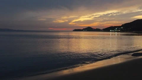 Gentle Waves on Sandy Beach Reflecting Orange Twilight Sky Stock Footage 345387665