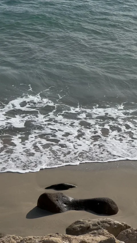 Gentle waves washing onto a sandy beach with smooth rocks and cliffs Stock Footage 297373581