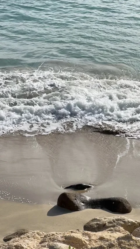 Gentle waves washing onto a sandy beach with smooth rocks in slow motion Stock Footage 297373583