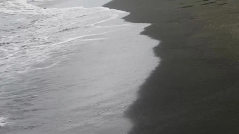 Gentle white foamy waves rhythmically rolling and washing across dark volcanic Vidéo 301919168
