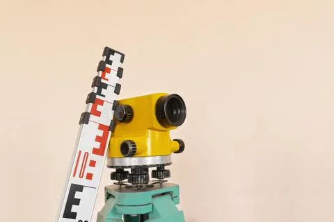 Geodesy level device on a tripod with ruler on the background a concrete pink Stock Photos
