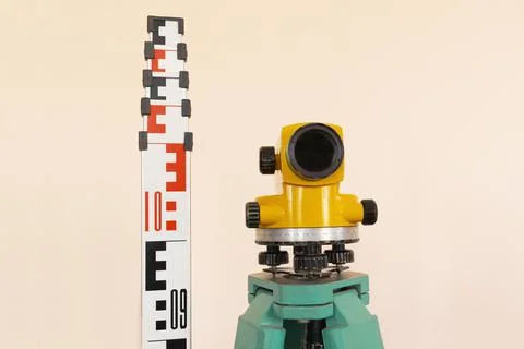 Geodesy level device on a tripod with ruler on the background a concrete pink Stock Photos