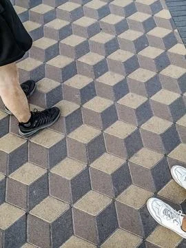 Geometric 3D cube pattern paving stones with people's feet in sneakers Stock Photos
