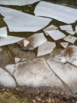 Geometric Broken Ice Chunks Floating on Shallow Brown Water Foto stock