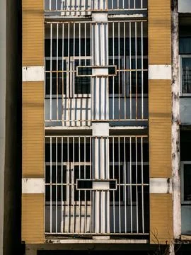 Geometric pattern of rusted white iron bar railings on yellow cladding apar.. Foto stock