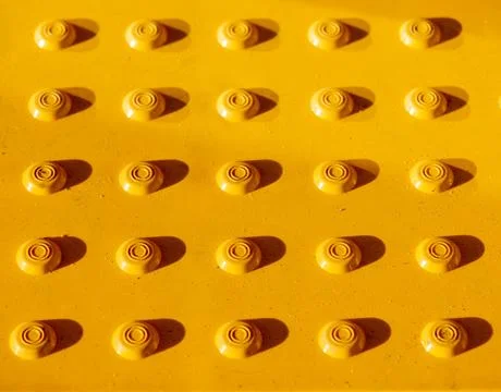 The geometric pattern of a yellow tactile warning tile for pedestrian safety on Stock Photos