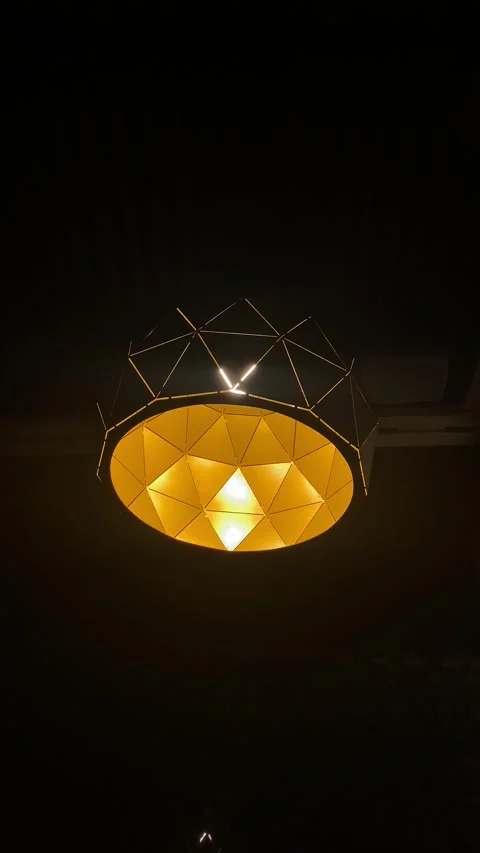 Geometric pendant lamp with triangular facet design sways gently in dark room Stock Footage 343790657