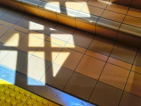 Geometric window frame shadow cast on yellow tiled floor with tactile paving Stock Photos