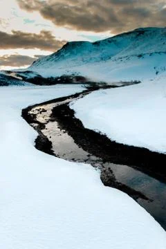 Geothermal black river with clouds and sky in white snow in Iceland Stock Photos