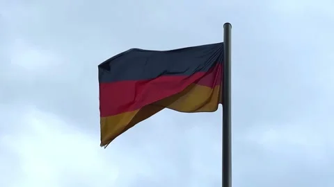 German flag waving proudly under a cloudy sky in an urban setting 動画素材 329320125