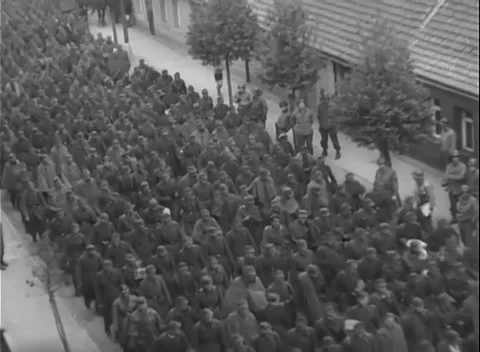 GERMANY - 1945: Tree trunks in foreground - Uniformed men fill a wide street Stock Footage 344598851
