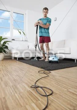 Germany, Augsburg, Man cleaning apartment with vacuum cleaner Stock Photos