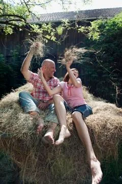 Germany, Bavaria, Couple sitting on haystack, fooling about, portrait Stock Photos