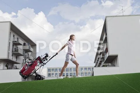 Germany, Bavaria, Munich, Young woman carrying golf cart Stock Photos