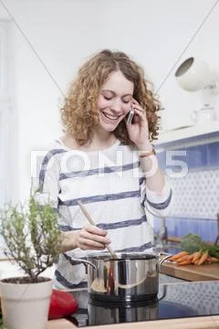 Germany, Bavaria, Munich, Young woman cooking and talking on phone in kitchen, Stock Photos