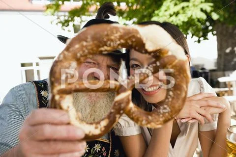 Germany, Bavaria, Upper Bavaria, Bavarian man and Asian woman holding pretzel, Stock Photos