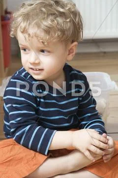 Germany, Berlin, Boy (3-4) sitting on wooden floor, looking away, portrait, Stock Photos