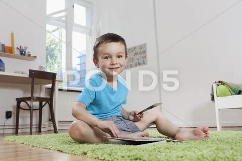 Germany, Berlin, Boy sitting on floor with book, smiling, portrait Stock Photos