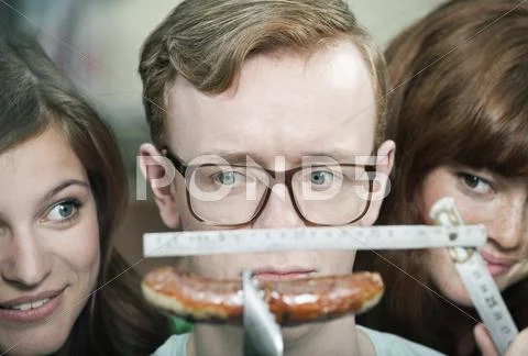 Germany, Berlin, Close up of young man measuring grilled sausage and women Stock Photos