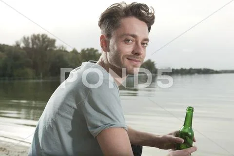 Germany, Berlin, Lake Wannsee, Young man holding bottle, smiling, portrait Stock Photos