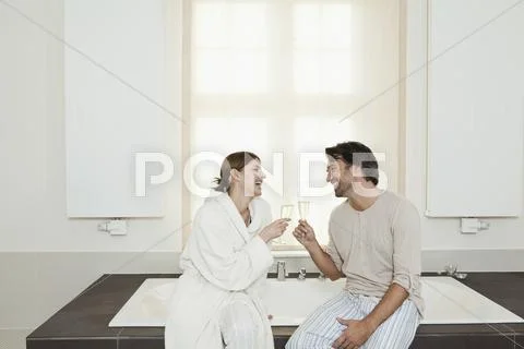 Germany, Berlin, Mature couple sitting on bathtub with sparkling wine Stock Photos