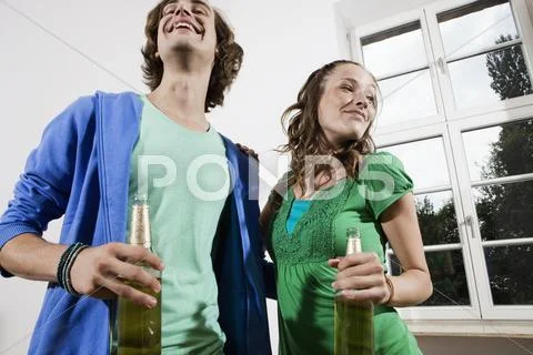 Germany, Berlin, Young couple holding beer bottles, laughing, portrait Stock Photos