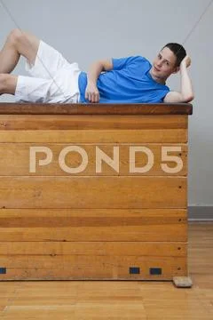 Germany, Berlin, Young man lying on vaulting horse, smiling, portrait Stock Photos