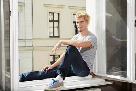 Germany, Berlin, Young man sitting at open window, smiling Stock Photos