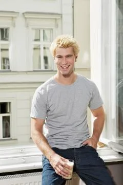Germany, Berlin, Young man sitting at open window, smiling Stock Photos