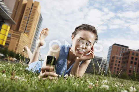 Germany, Berlin, Young woman lying in meadow, using mobile phone, portrait Stock Photos