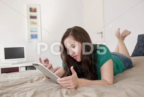 Germany, Berlin, Young Woman Lying On Bed And Using Digital Tablet
