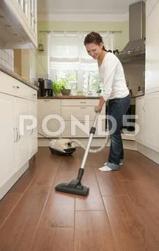 Germany, Brandenburg, Young woman cleaning floor with vacuum cleaner Stock Photos