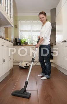 Germany, Brandenburg, Young woman cleaning floor with vacuum cleaner Stock Photos