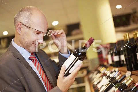 Germany, Cologne, Mature man inspecting wine bottle in supermarket Stock Photos