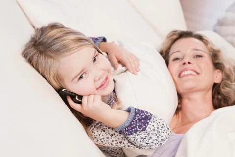 Germany, Cologne, Mother lying on sofa, daughter (4-5) using mobile phone, Stock Photos