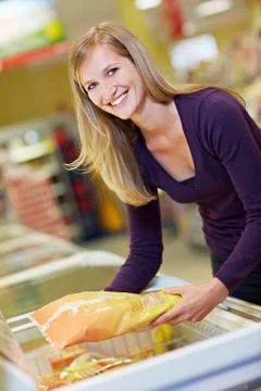 Germany, Cologne, Young woman standing at freezer in supermarket Stock Photos