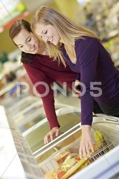 Germany, Cologne, Young women at freezer in supermarket Stock Photos