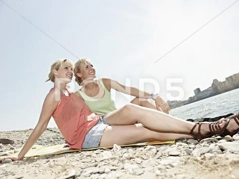 Germany, Cologne, Young women sitting on riverbank Stock Photos