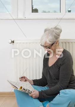Germany, Duesseldorf, Woman solving crossword near heater Stock Photos