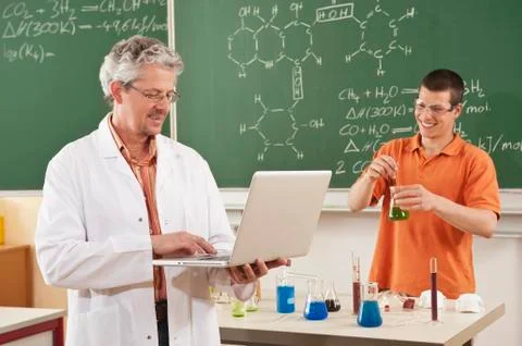 Germany, Emmering, Man using laptop with young man doing experiment in Stock Photos