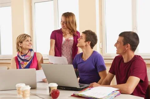 Germany, Emmering, Students using laptop with disposable cup and apple on table 写真素材