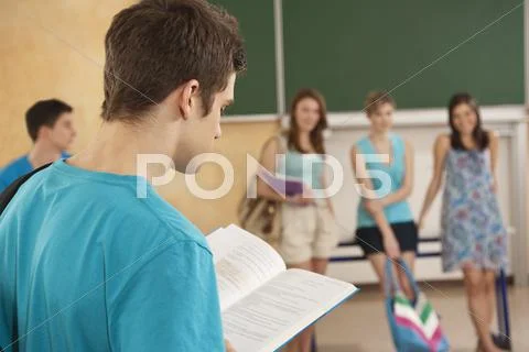 Germany, Emmering, Teenage boy reading book with students in background Stock-Fotos