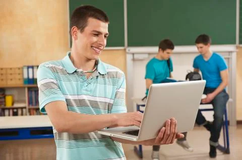 Germany, Emmering, Young man using laptop with students in background Stock Photos