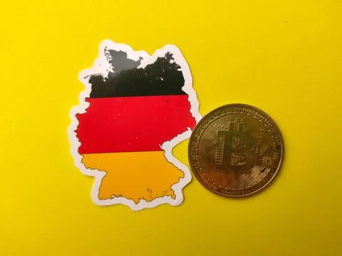 Germany flag-colored map sticker next to a gold Bitcoin physical coin on a .. Stock Photos