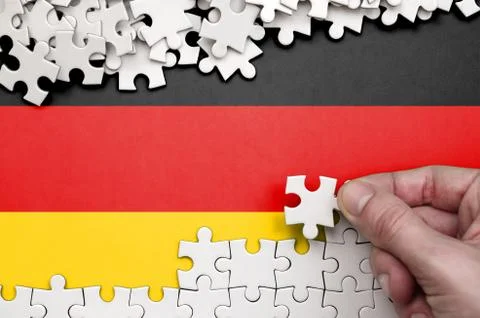 Germany flag  is depicted on a table on which the human hand folds a puzzle o Foto stock